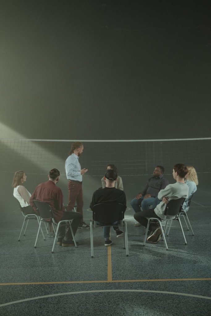 Demo Post 1 Adults participating in a group therapy session in a gymnasium, promoting mental health and peer support.
